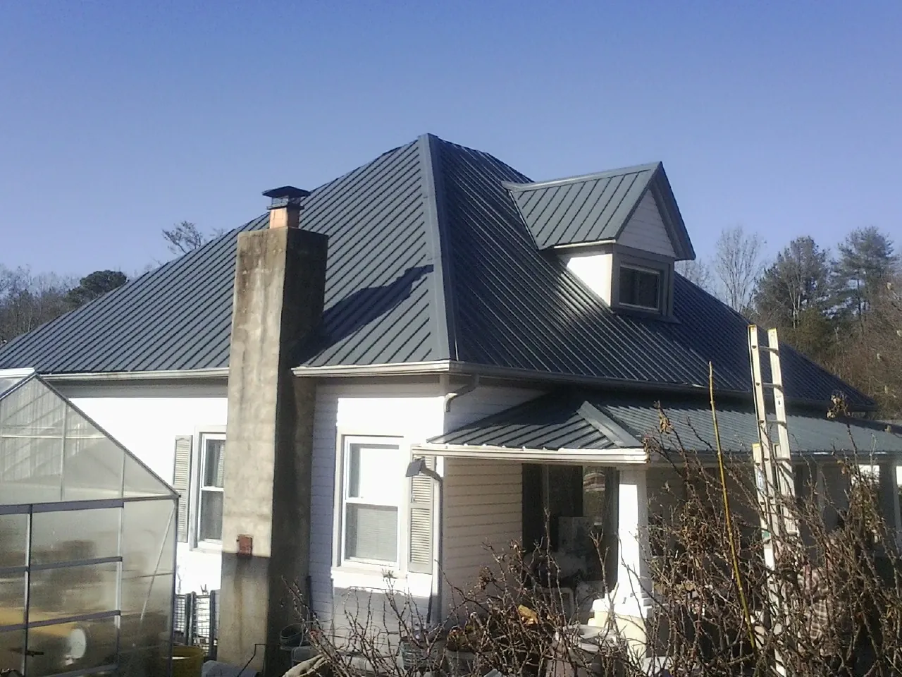 Dark blue standing seam metal roof on a white farmhouse with dormer — Slate & Tile Roof Repair by Roofing Brothers in Little Suamico
