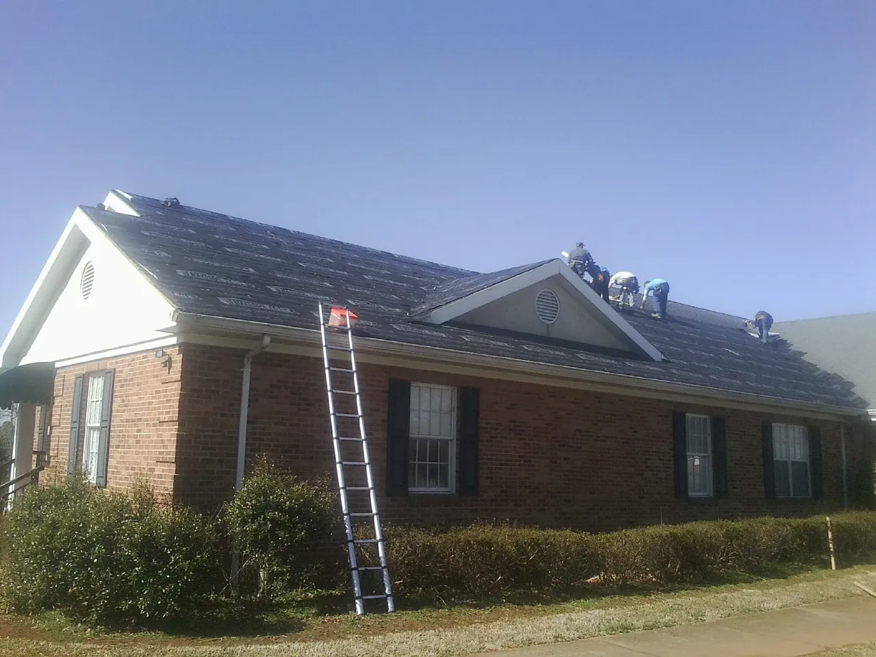 Crew tearing shingles off a brick ranch roof with a ladder set — Metal Roof Repair work by our crew in Little Suamico