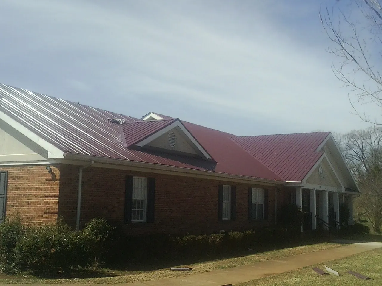Red metal roof with gabled entries on a long brick building, from a Hail Damage Roof Repair job in Little Suamico