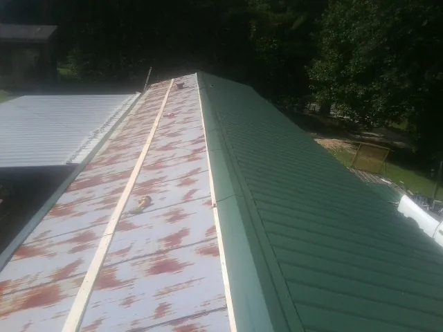 Old rusted panels beside newly installed green metal roofing — Wind Damage Roof Repair by Roofing Brothers in Little Suamico