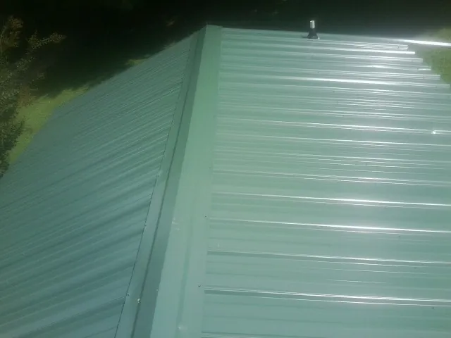 New green metal panels meeting at the ridge of a roof — Flat Roof Repair work by our crew in Little Suamico