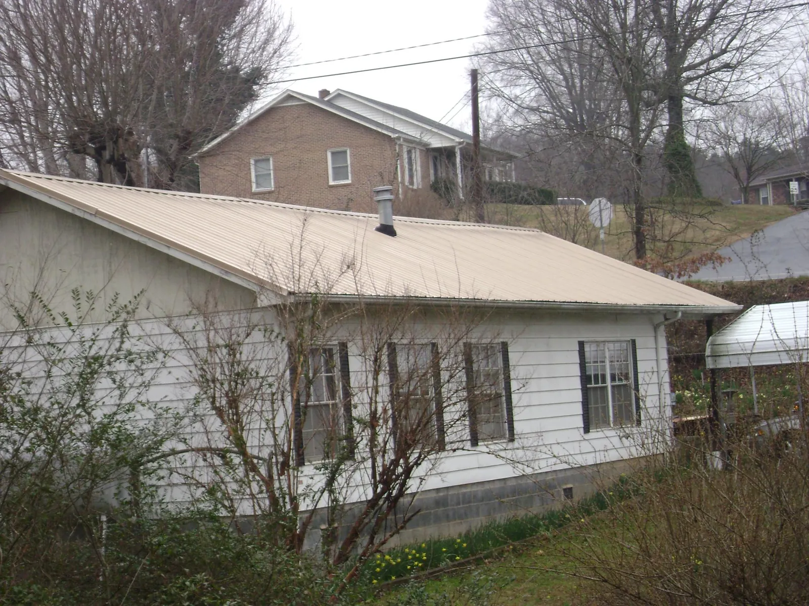 Tan metal roof on a white sided house set into a hillside — Commercial Roofing by Roofing Brothers in Little Suamico