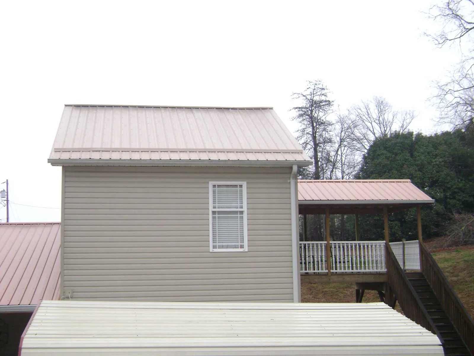 Tan metal roofs on a two story addition and attached porch, from a Roof Replacement job in Little Suamico